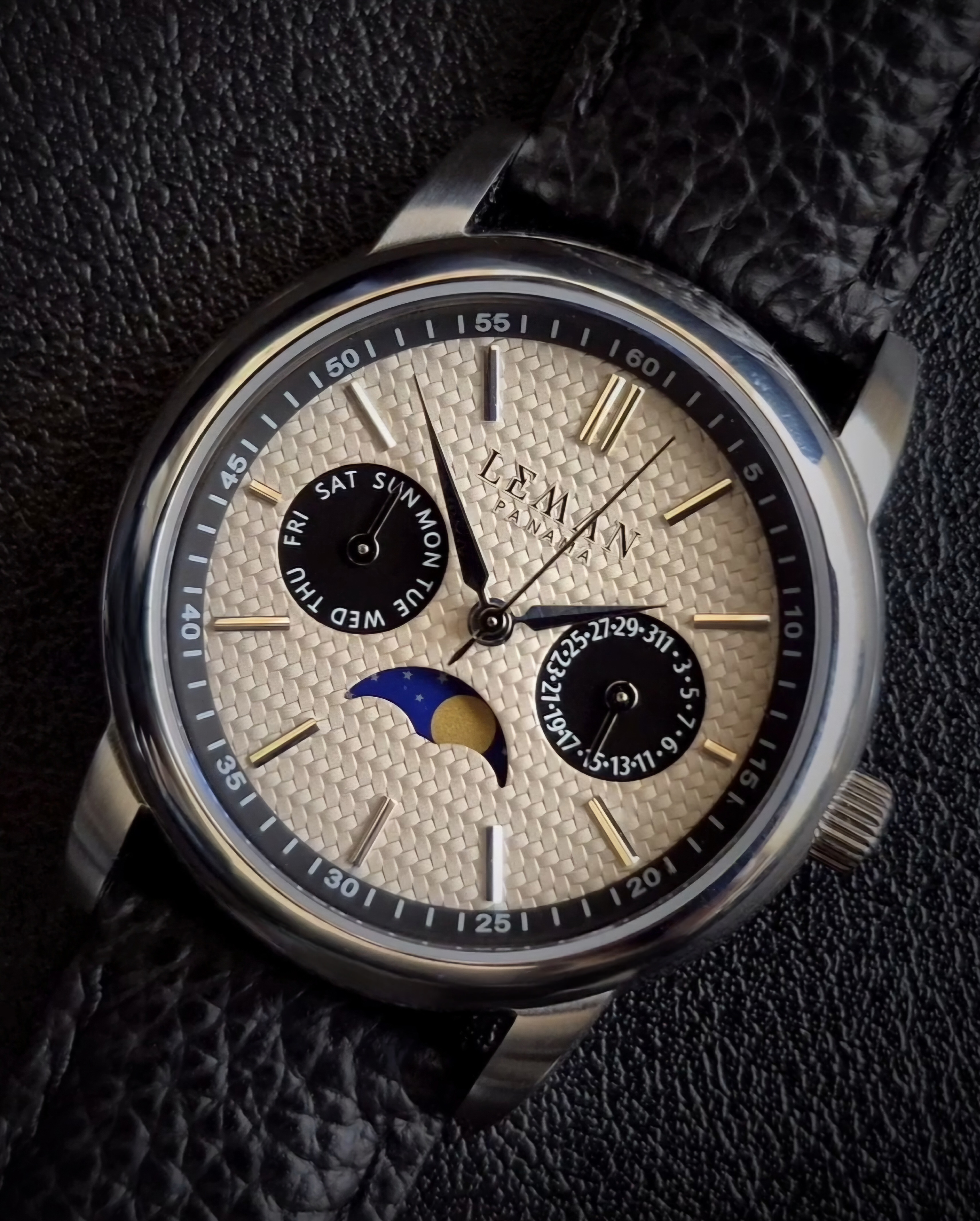 Leman Panama moonsphase watch close-up image against a black leather background featuring a black leather strap